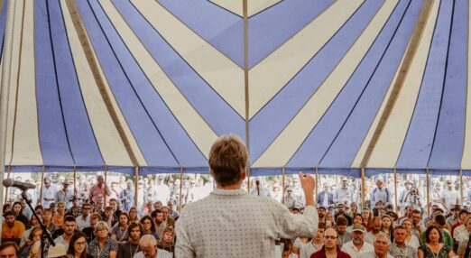 Speaker presents to a crowd under a bell tent